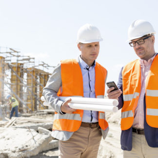 Architect and project manager looking at a mobile phone whilst standing on a construction site