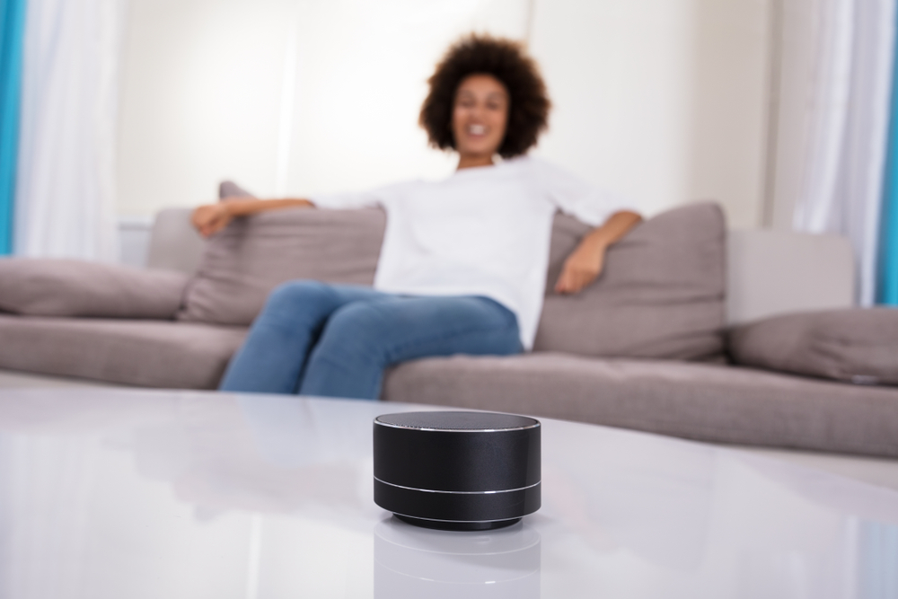 Voice assistant in smart device on coffee table with user sat on sofa