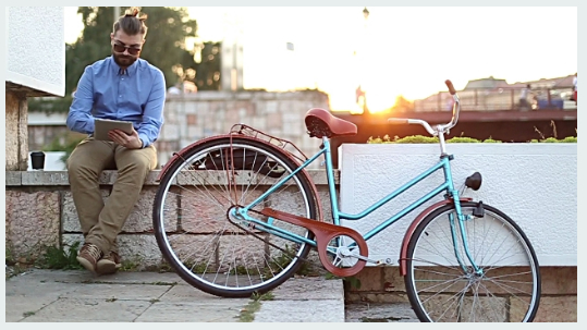Hipster using tablet with top knot, beard and bike, sunset effect